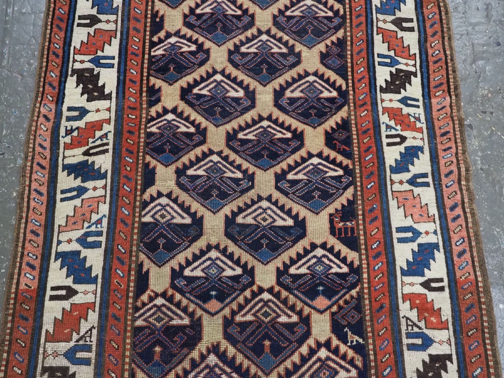 An antique Caucasian wool rug runner featuring a central geometric lattice pattern in navy blue and cream within multiple decorative borders. View V