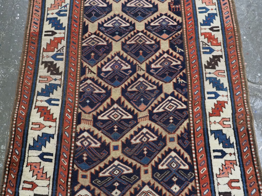 An antique Caucasian wool rug runner featuring a central geometric lattice pattern in navy blue and cream within multiple decorative borders. View VI