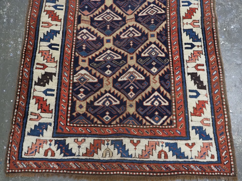 An antique Caucasian wool rug runner featuring a central geometric lattice pattern in navy blue and cream within multiple decorative borders. View VII