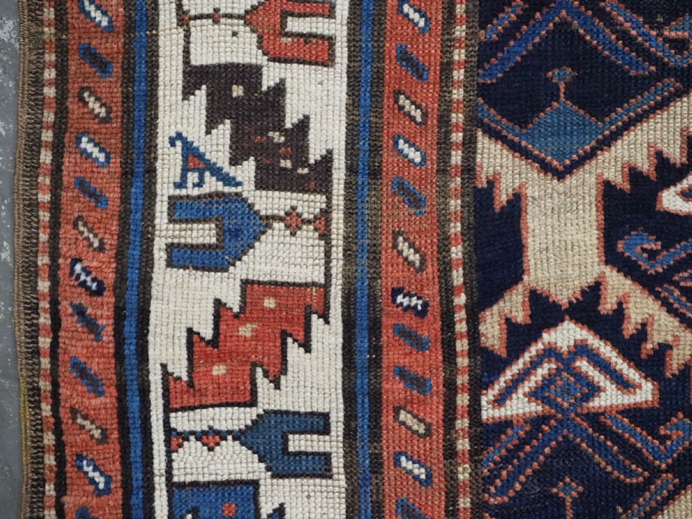 An antique Caucasian wool rug runner featuring a central geometric lattice pattern in navy blue and cream within multiple decorative borders. View IX