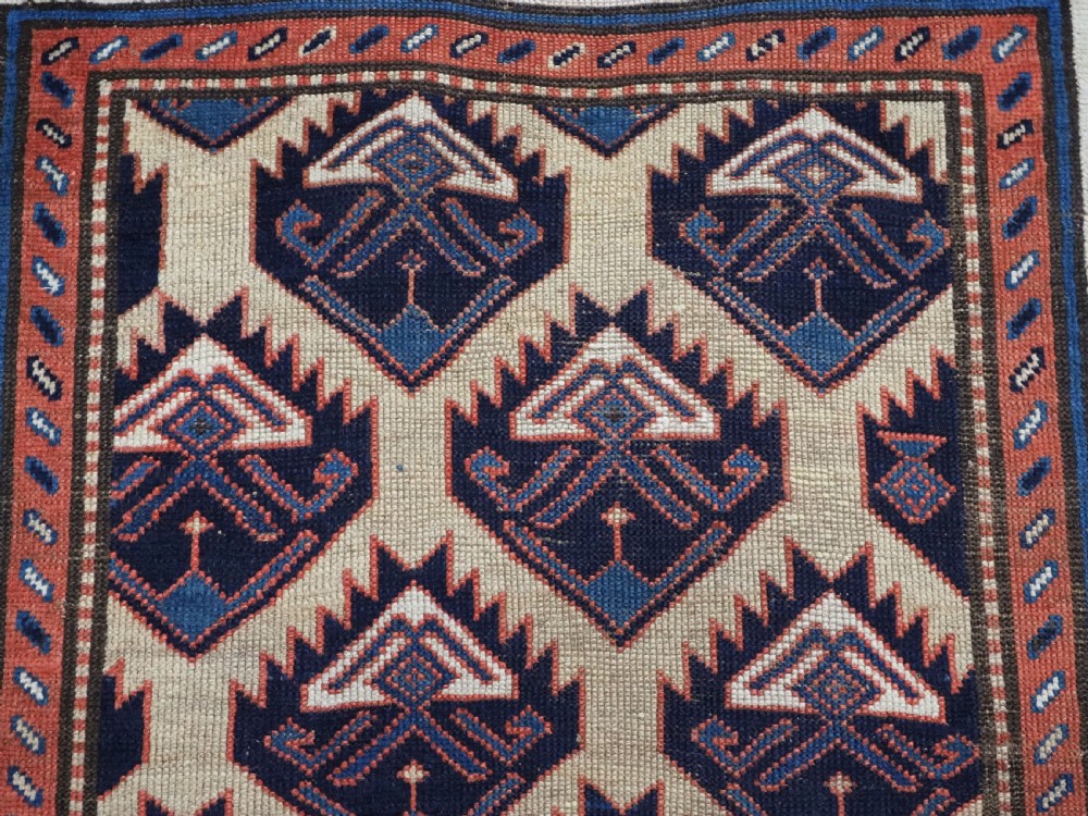 An antique Caucasian wool rug runner featuring a central geometric lattice pattern in navy blue and cream within multiple decorative borders. View X