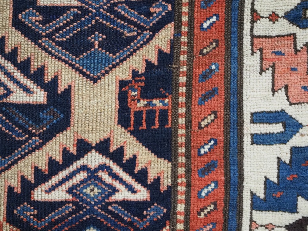 An antique Caucasian wool rug runner featuring a central geometric lattice pattern in navy blue and cream within multiple decorative borders. View XII