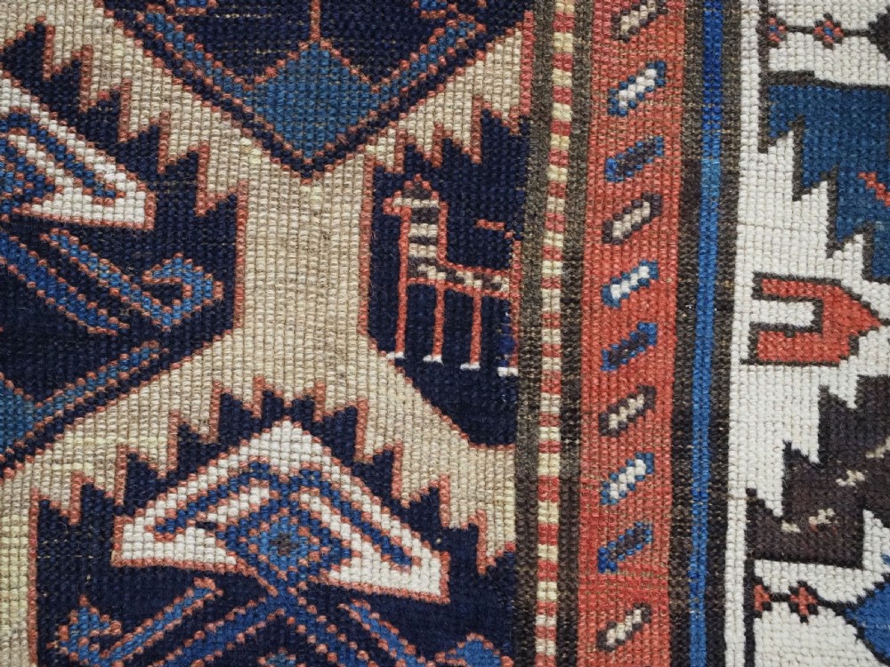 An antique Caucasian wool rug runner featuring a central geometric lattice pattern in navy blue and cream within multiple decorative borders. View XIII