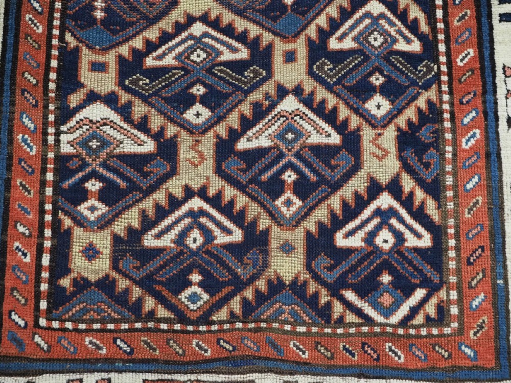An antique Caucasian wool rug runner featuring a central geometric lattice pattern in navy blue and cream within multiple decorative borders. View XIV