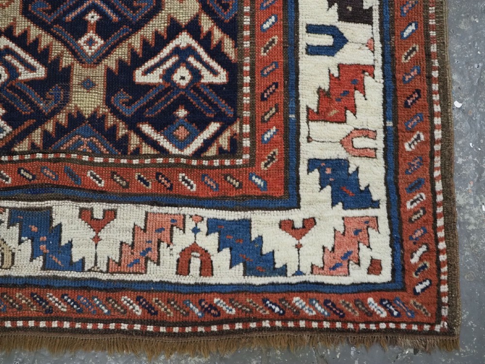 An antique Caucasian wool rug runner featuring a central geometric lattice pattern in navy blue and cream within multiple decorative borders. View XV