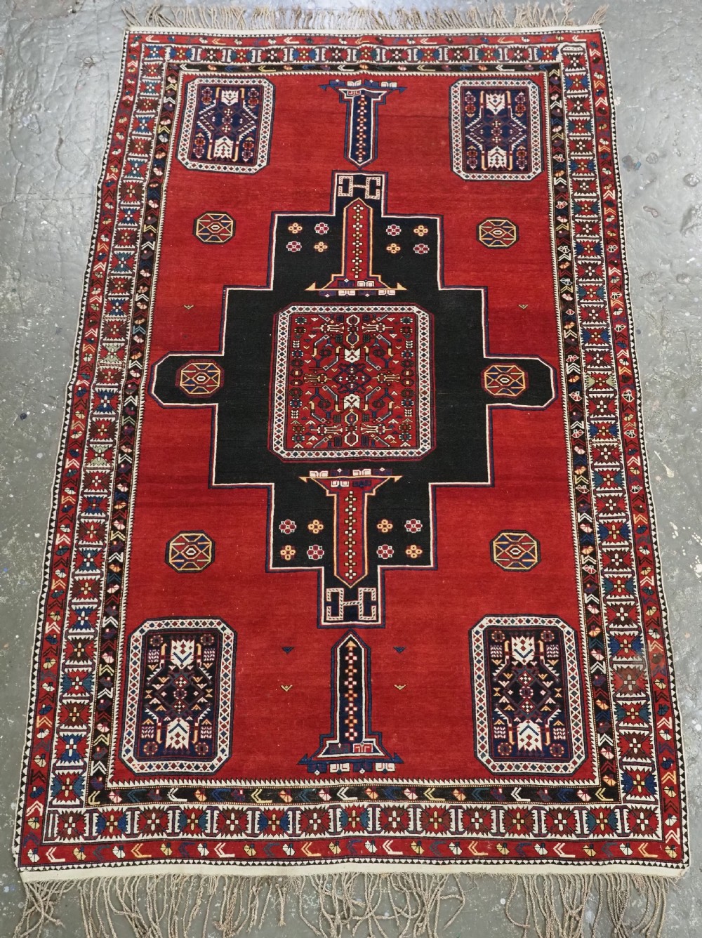 An antique Caucasian Konagkend hand-knotted wool rug featuring a large dark cruciform central medallion on a deep red ground with geometric borders and fringe.