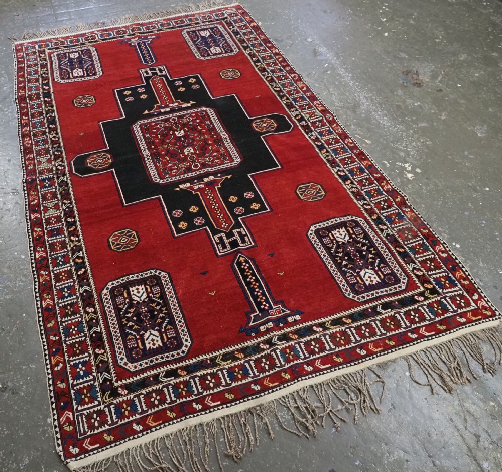 An antique Caucasian Konagkend hand-knotted wool rug featuring a large dark cruciform central medallion on a deep red ground with geometric borders and fringe. View II