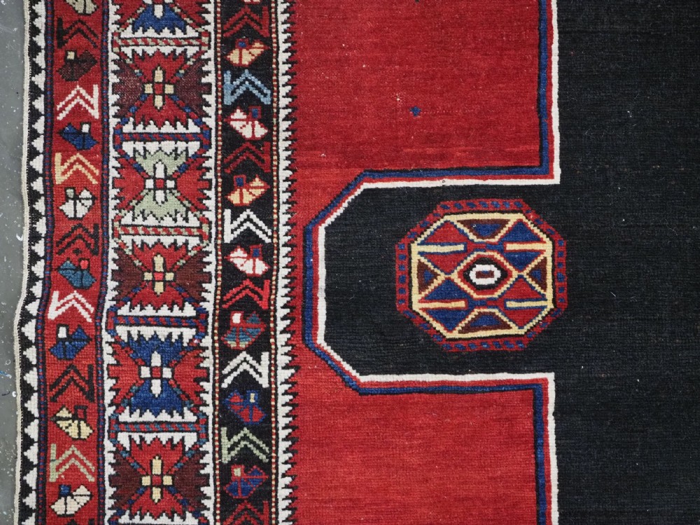 An antique Caucasian Konagkend hand-knotted wool rug featuring a large dark cruciform central medallion on a deep red ground with geometric borders and fringe. View VI