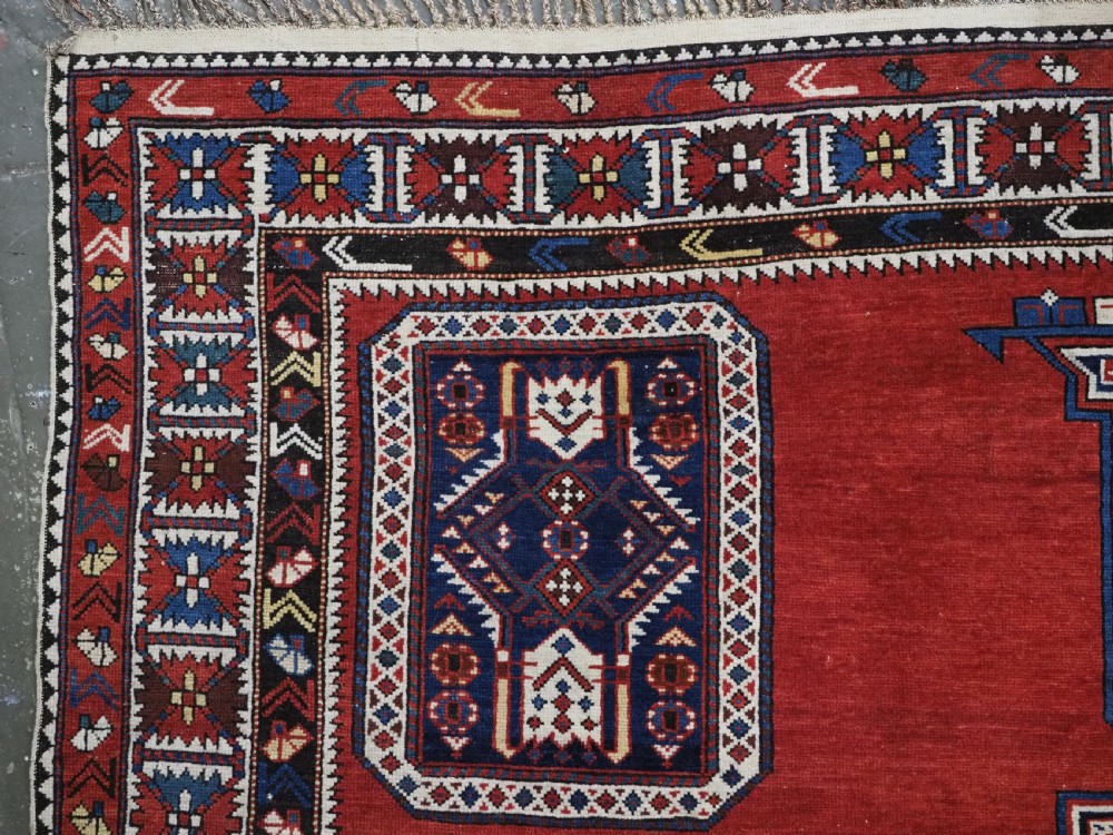 An antique Caucasian Konagkend hand-knotted wool rug featuring a large dark cruciform central medallion on a deep red ground with geometric borders and fringe. View VII