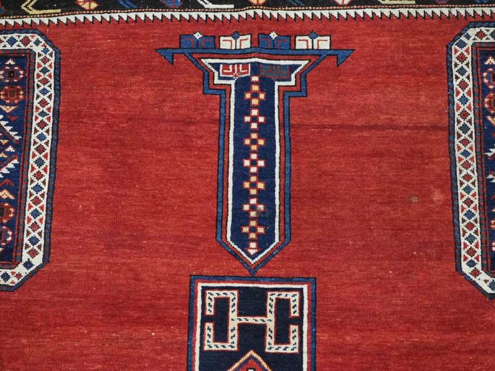 An antique Caucasian Konagkend hand-knotted wool rug featuring a large dark cruciform central medallion on a deep red ground with geometric borders and fringe. View VIII