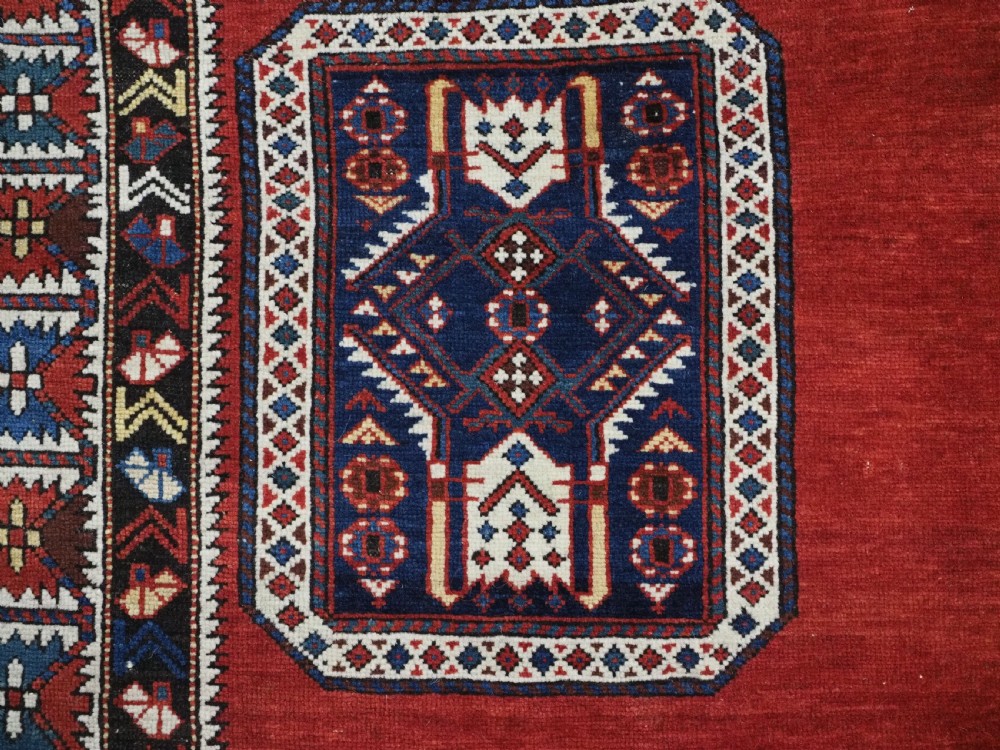 An antique Caucasian Konagkend hand-knotted wool rug featuring a large dark cruciform central medallion on a deep red ground with geometric borders and fringe. View IX