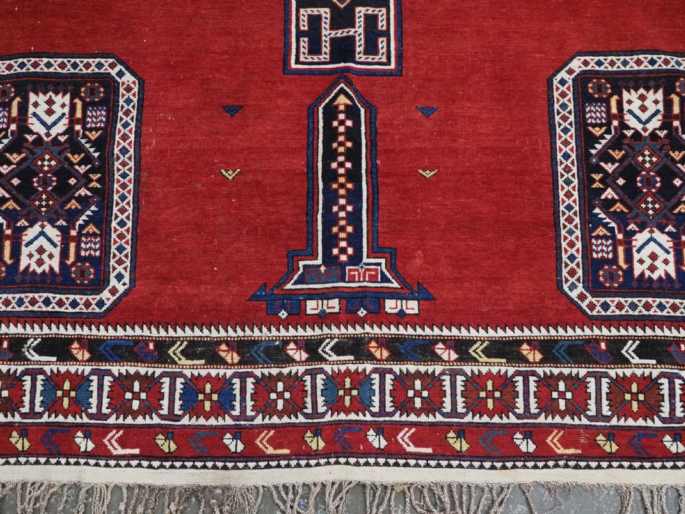 An antique Caucasian Konagkend hand-knotted wool rug featuring a large dark cruciform central medallion on a deep red ground with geometric borders and fringe. View XIII