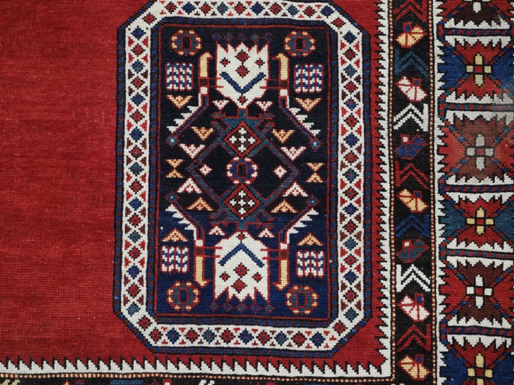 An antique Caucasian Konagkend hand-knotted wool rug featuring a large dark cruciform central medallion on a deep red ground with geometric borders and fringe. View XIV