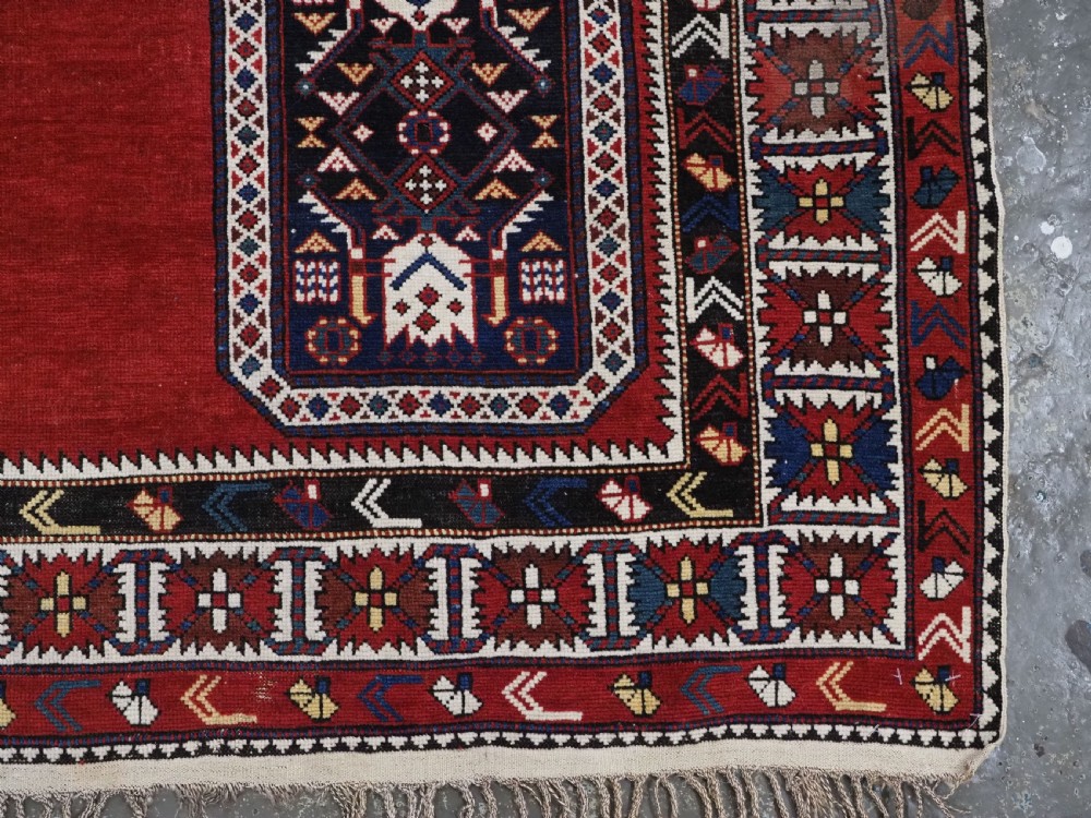 An antique Caucasian Konagkend hand-knotted wool rug featuring a large dark cruciform central medallion on a deep red ground with geometric borders and fringe. View XV