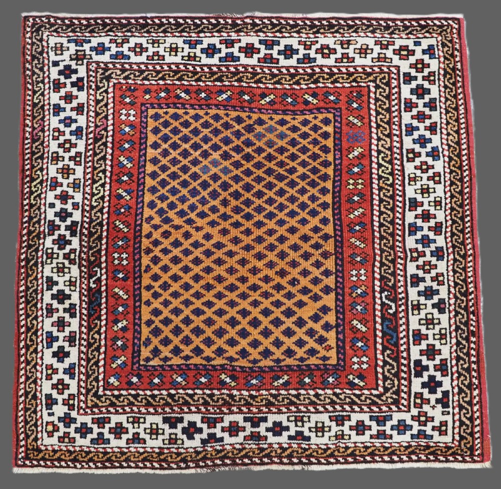 A small square antique hand-knotted wool rug featuring a mustard yellow lattice central field surrounded by red and ivory geometric borders.