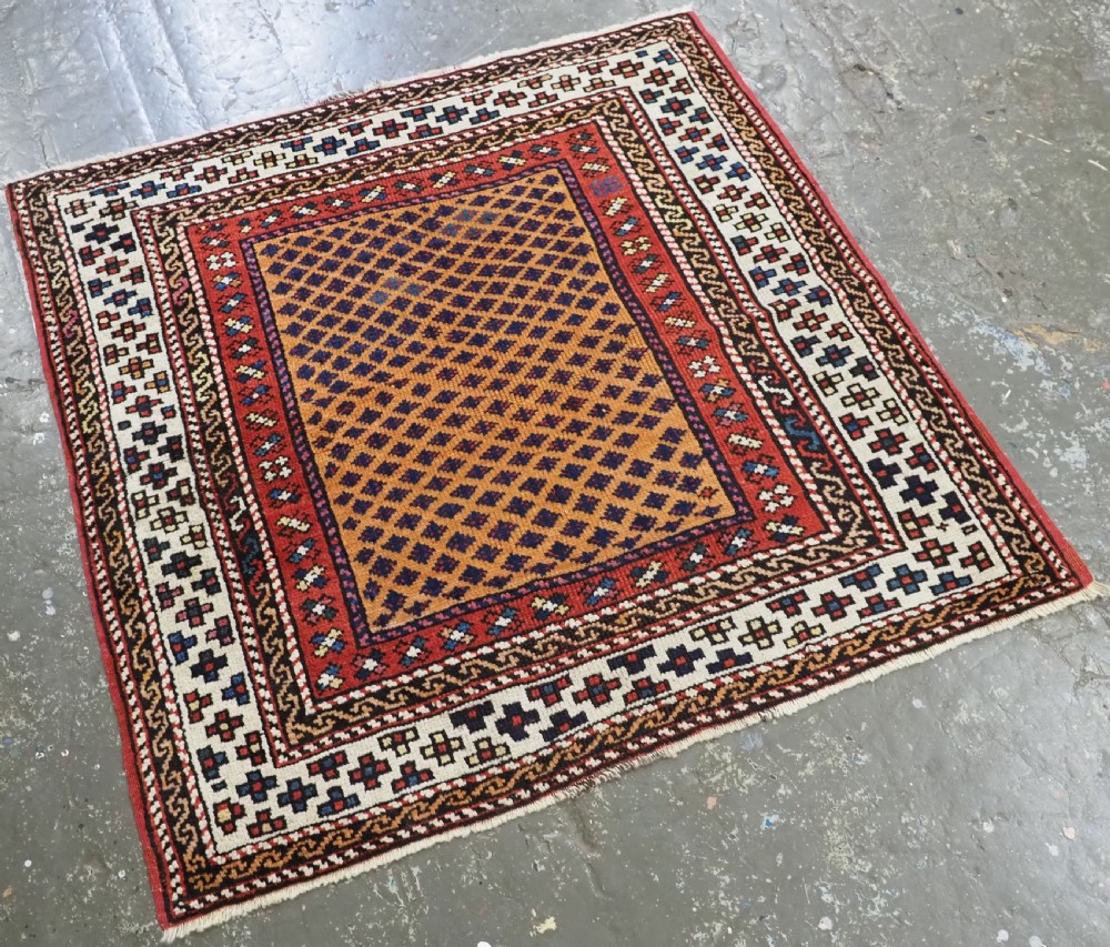 A small square antique hand-knotted wool rug featuring a mustard yellow lattice central field surrounded by red and ivory geometric borders. View II