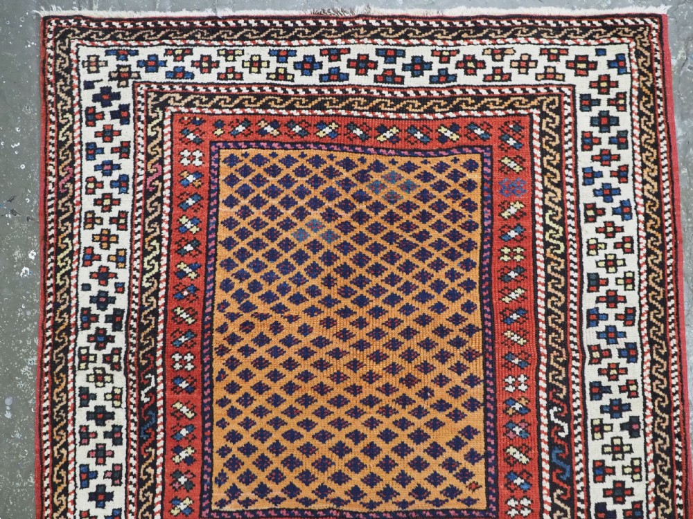 A small square antique hand-knotted wool rug featuring a mustard yellow lattice central field surrounded by red and ivory geometric borders. View III