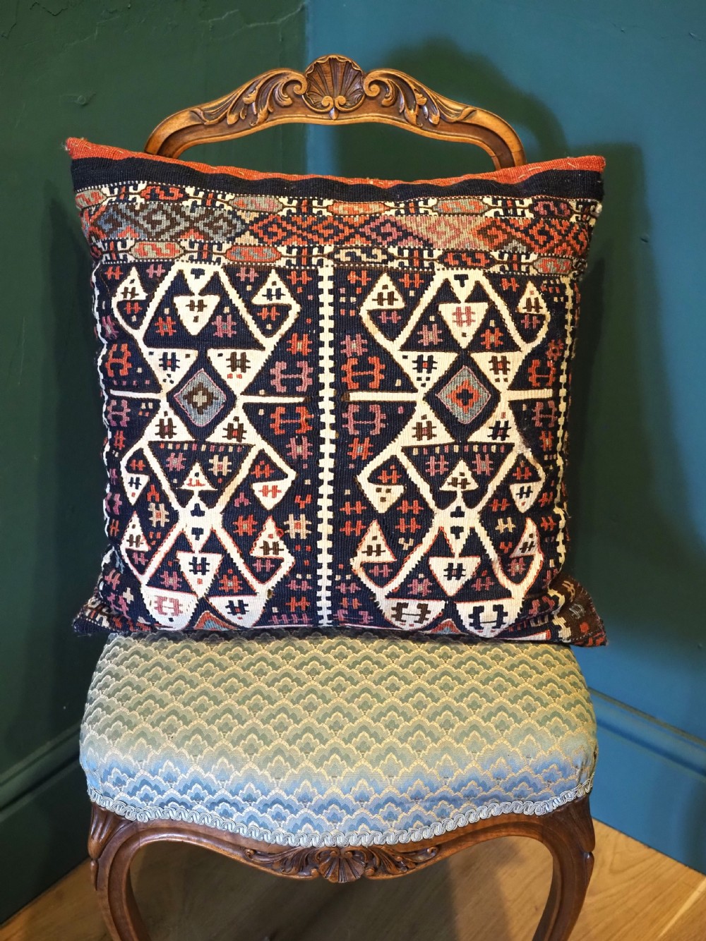 A square hand-woven wool kilim cushion featuring geometric Anatolian patterns in navy blue, off-white, and terracotta.