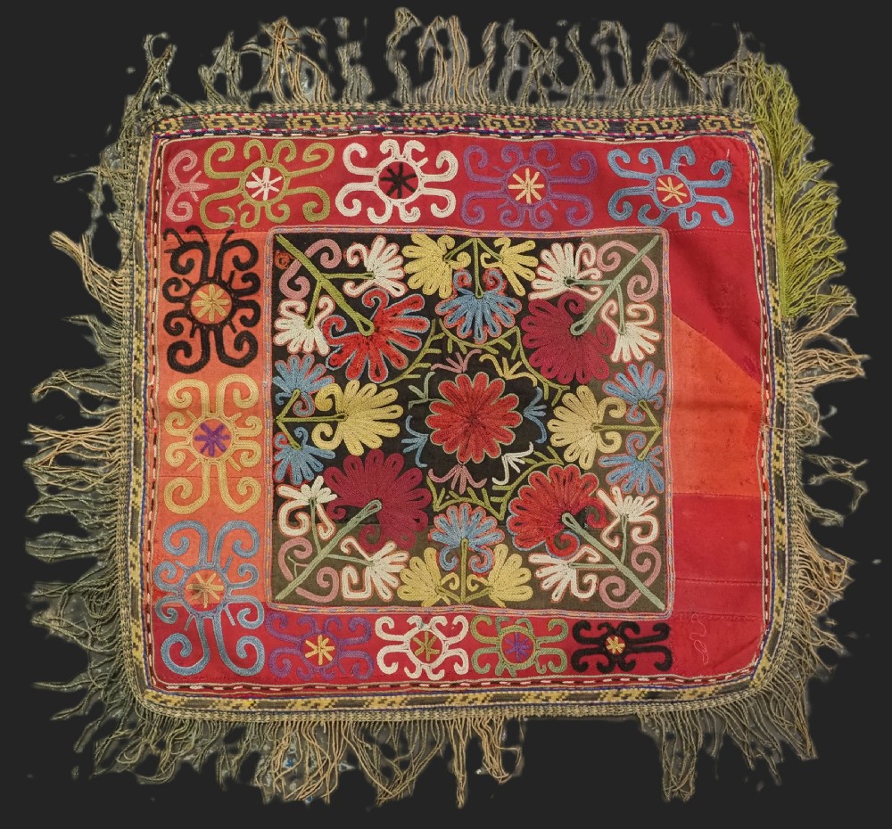 A square antique Uzbek Lakai tribe ilgich embroidery featuring multi-coloured floral and scroll motifs on a red background with fringed edges. View II