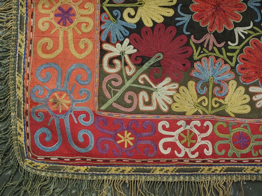 A square antique Uzbek Lakai tribe ilgich embroidery featuring multi-coloured floral and scroll motifs on a red background with fringed edges. View IV