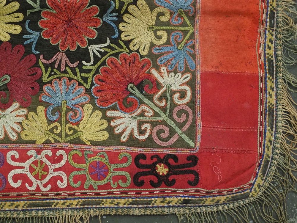 A square antique Uzbek Lakai tribe ilgich embroidery featuring multi-coloured floral and scroll motifs on a red background with fringed edges. View VI