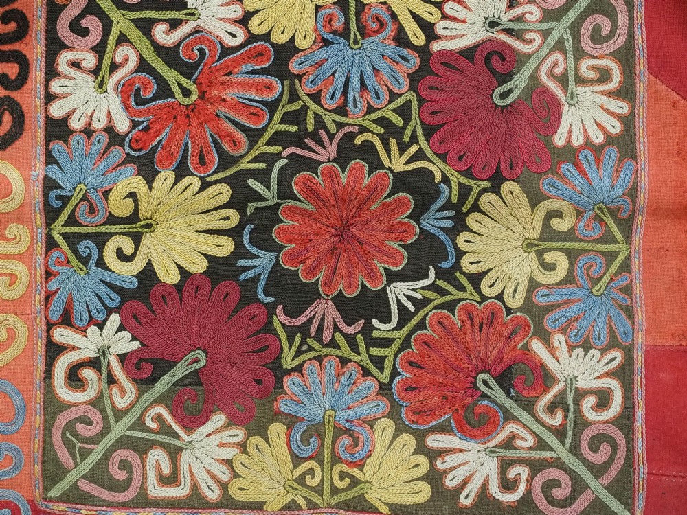 A square antique Uzbek Lakai tribe ilgich embroidery featuring multi-coloured floral and scroll motifs on a red background with fringed edges. View VII