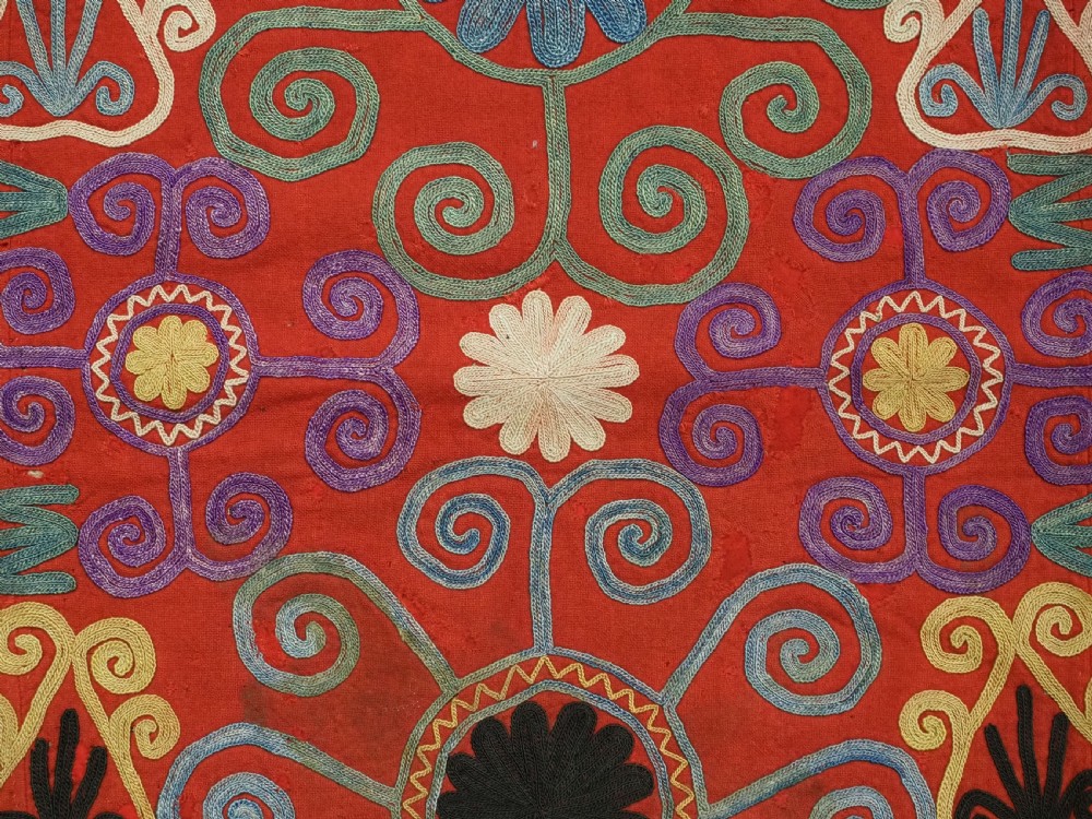 A shield-shaped red Central Asian textile featuring dense silk embroidery with swirling scroll motifs and floral rosettes. View VI
