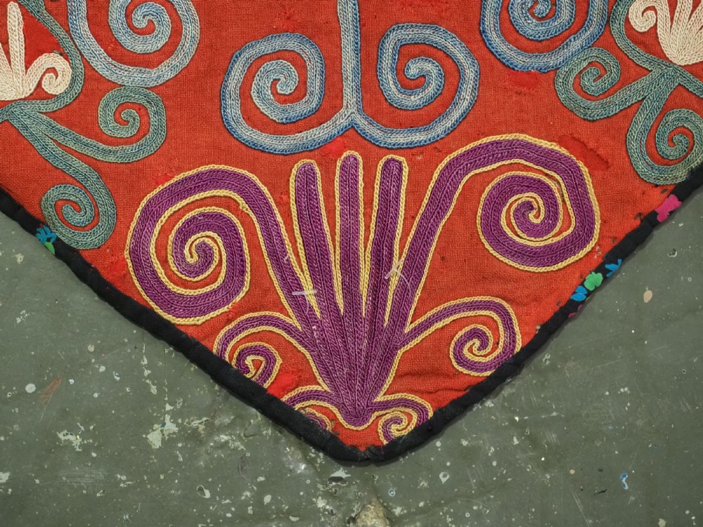 A shield-shaped red Central Asian textile featuring dense silk embroidery with swirling scroll motifs and floral rosettes. View VIII