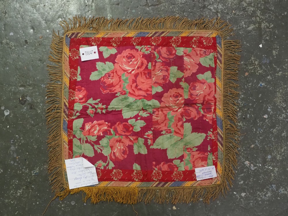 A square red embroidered textile featuring bold central circular motifs, tribal geometric shapes, and a fringed outer border. View VIII