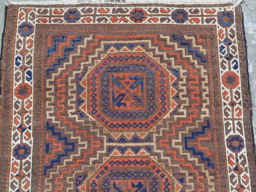 An antique hand-knotted wool rug featuring four central octagonal guls framed by stepped geometric borders in dark brown, terracotta, blue, and cream hues. View III