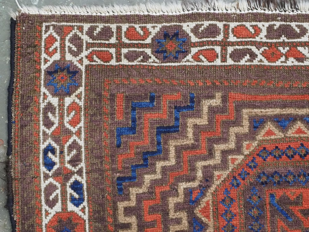 An antique hand-knotted wool rug featuring four central octagonal guls framed by stepped geometric borders in dark brown, terracotta, blue, and cream hues. View VI