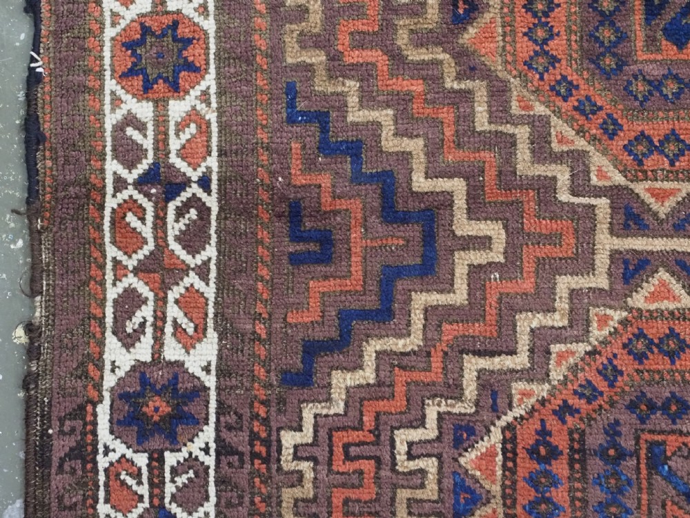 An antique hand-knotted wool rug featuring four central octagonal guls framed by stepped geometric borders in dark brown, terracotta, blue, and cream hues. View VII