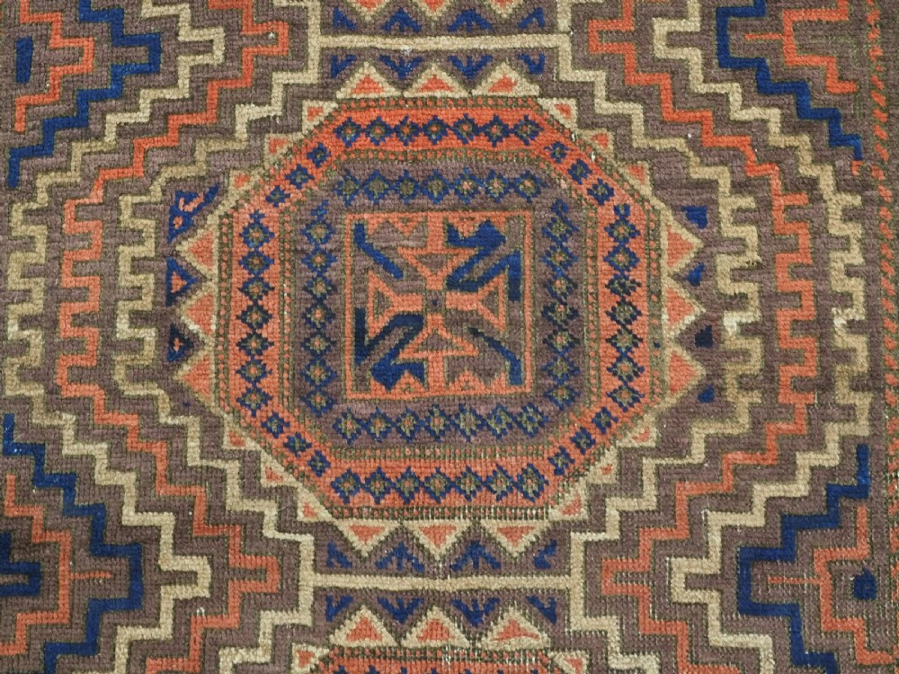 An antique hand-knotted wool rug featuring four central octagonal guls framed by stepped geometric borders in dark brown, terracotta, blue, and cream hues. View IX