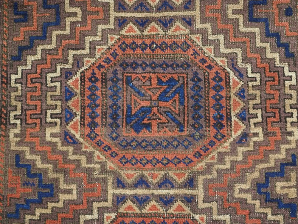 An antique hand-knotted wool rug featuring four central octagonal guls framed by stepped geometric borders in dark brown, terracotta, blue, and cream hues. View X