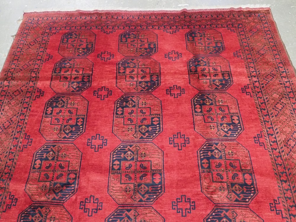 A hand-knotted antique Afghan wool carpet in warm red featuring dark blue repeating octagonal gul motifs and geometric borders. View III