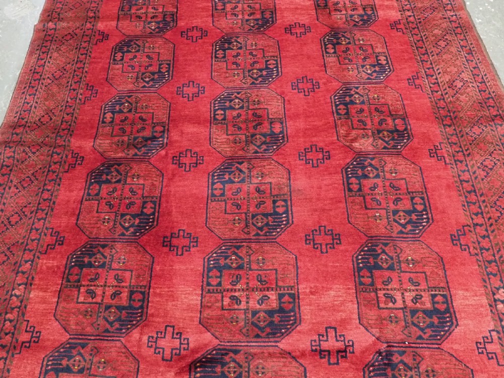 A hand-knotted antique Afghan wool carpet in warm red featuring dark blue repeating octagonal gul motifs and geometric borders. View IV