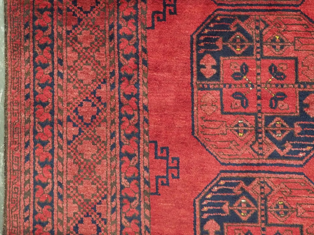A hand-knotted antique Afghan wool carpet in warm red featuring dark blue repeating octagonal gul motifs and geometric borders. View VII