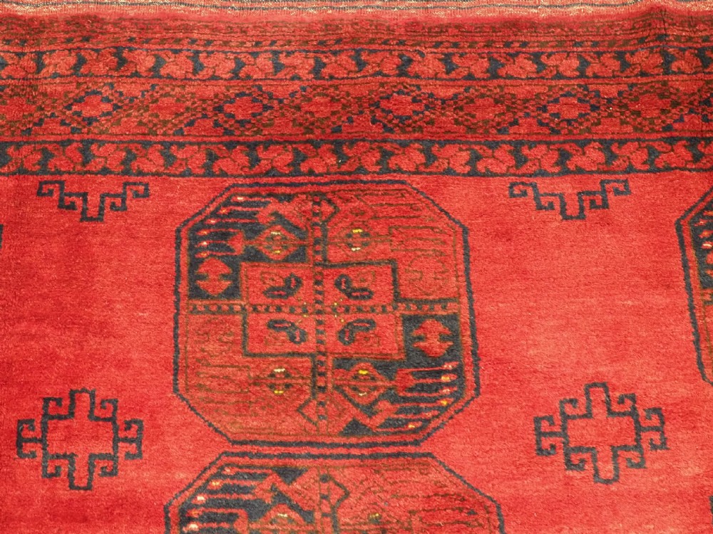 A hand-knotted antique Afghan wool carpet in warm red featuring dark blue repeating octagonal gul motifs and geometric borders. View VIII