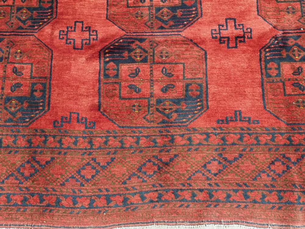 A hand-knotted antique Afghan wool carpet in warm red featuring dark blue repeating octagonal gul motifs and geometric borders. View XI