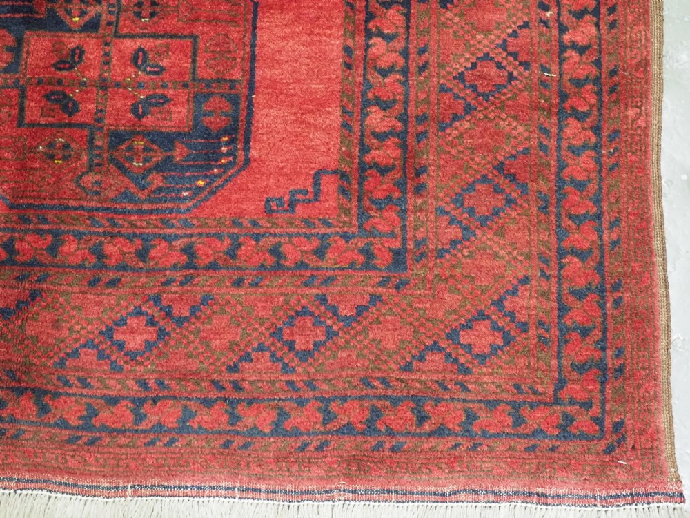 A hand-knotted antique Afghan wool carpet in warm red featuring dark blue repeating octagonal gul motifs and geometric borders. View XII