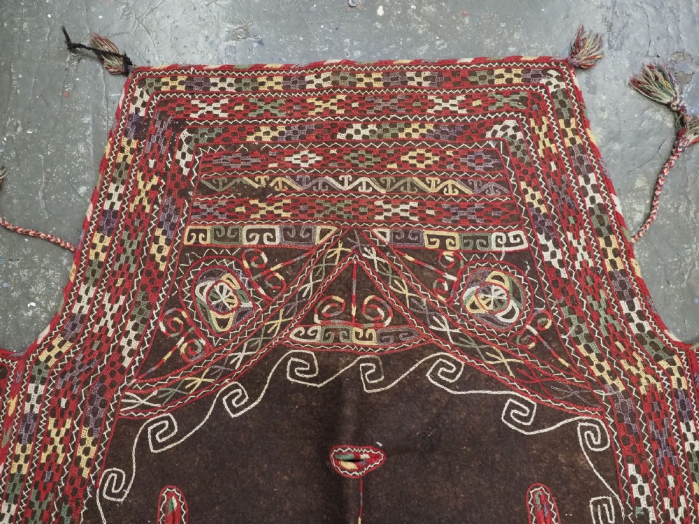 An antique Yomut Turkmen dark brown felt horse blanket featuring intricate red, cream, and green geometric embroidered borders, central spiral scroll motifs, and top corner tassels. View II