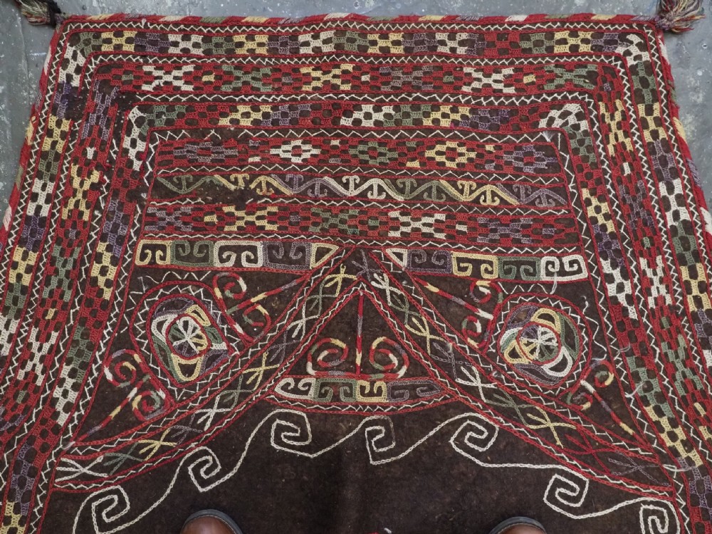 An antique Yomut Turkmen dark brown felt horse blanket featuring intricate red, cream, and green geometric embroidered borders, central spiral scroll motifs, and top corner tassels. View V