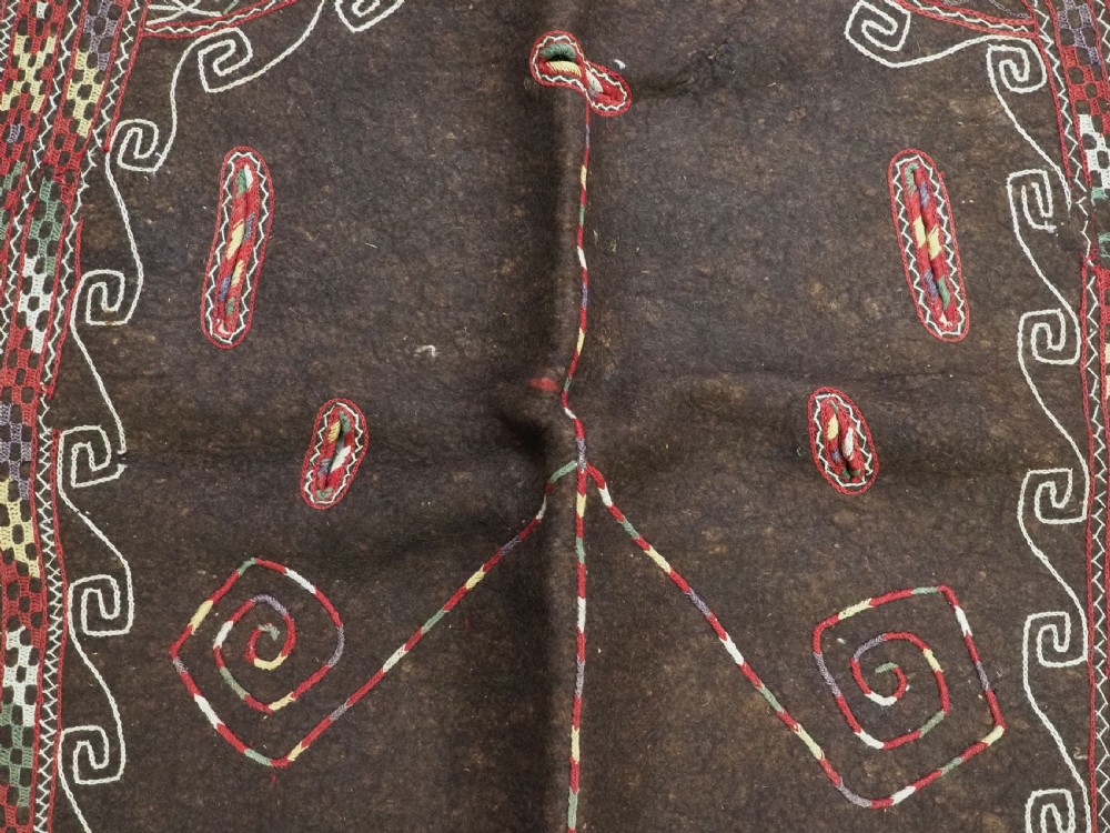An antique Yomut Turkmen dark brown felt horse blanket featuring intricate red, cream, and green geometric embroidered borders, central spiral scroll motifs, and top corner tassels. View IX