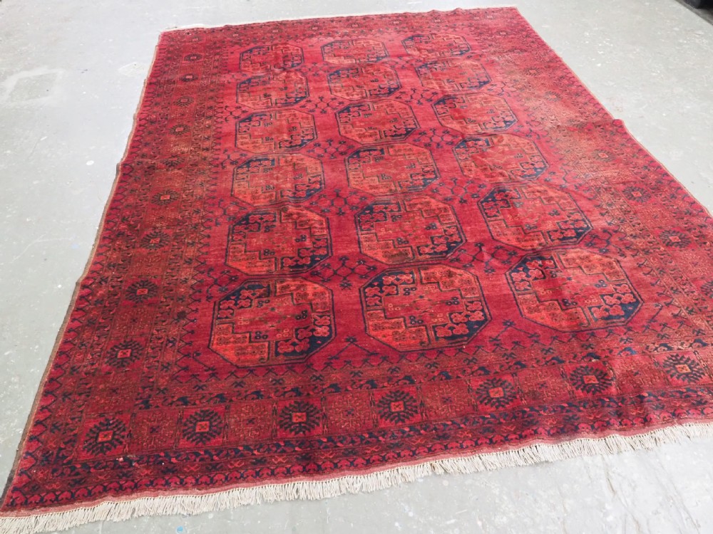 An antique hand-knotted Afghan Ersari wool carpet featuring dark blue octagonal gul motifs arranged in rows on a warm red field. View II