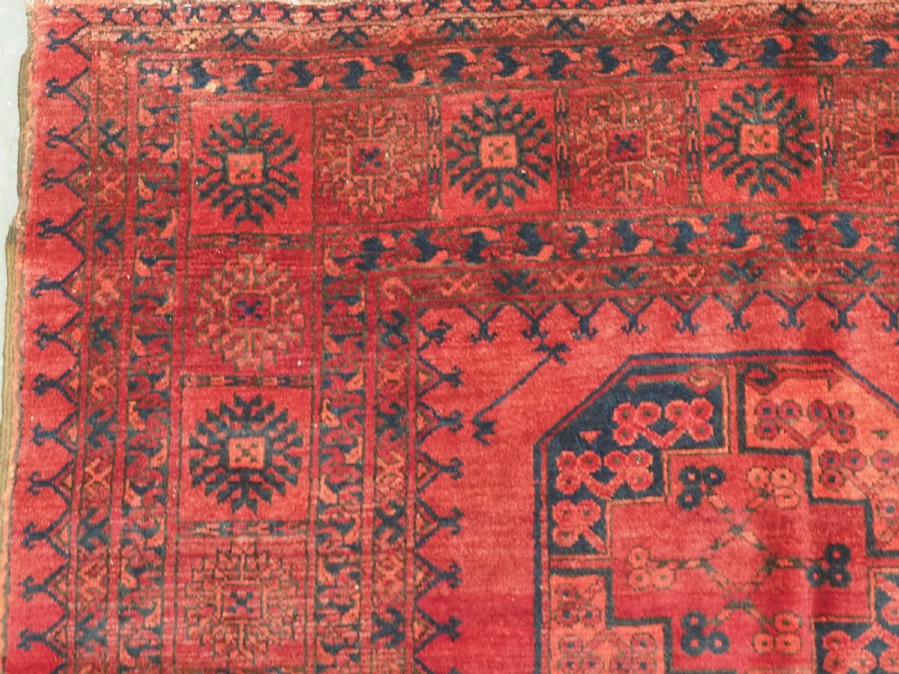 An antique hand-knotted Afghan Ersari wool carpet featuring dark blue octagonal gul motifs arranged in rows on a warm red field. View VI