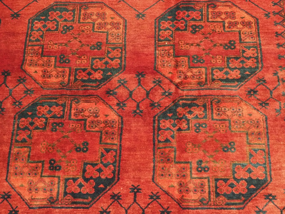 An antique hand-knotted Afghan Ersari wool carpet featuring dark blue octagonal gul motifs arranged in rows on a warm red field. View VIII