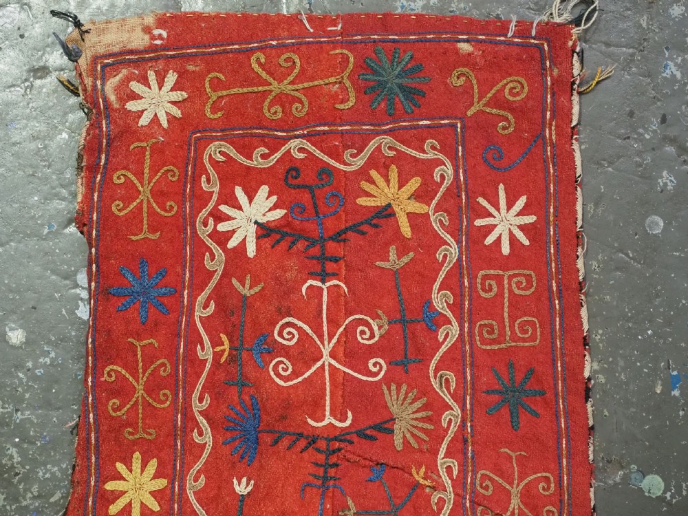 A vibrant red wool embroidered tribal textile bag featuring intricate polychrome scroll motifs in yellow, blue, purple, and green, finished with tassels at the bottom corners. View VIII