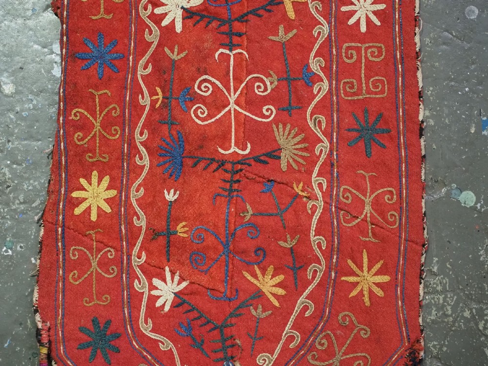 A vibrant red wool embroidered tribal textile bag featuring intricate polychrome scroll motifs in yellow, blue, purple, and green, finished with tassels at the bottom corners. View IX