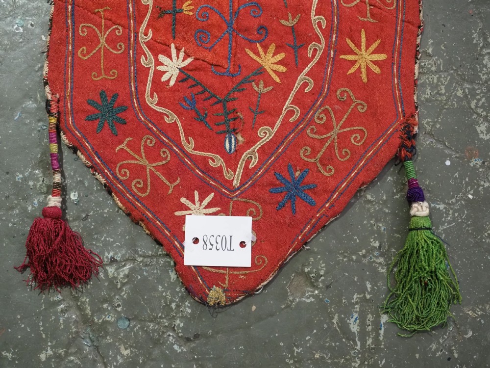 A vibrant red wool embroidered tribal textile bag featuring intricate polychrome scroll motifs in yellow, blue, purple, and green, finished with tassels at the bottom corners. View X
