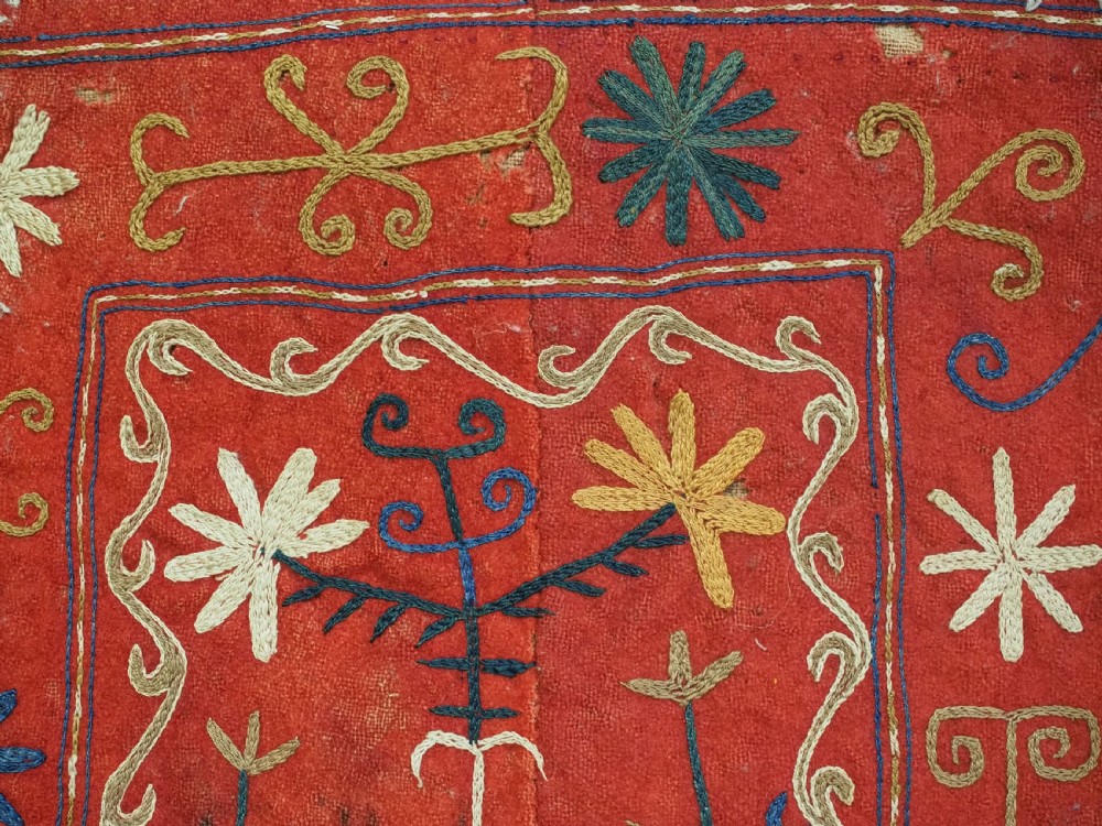 A vibrant red wool embroidered tribal textile bag featuring intricate polychrome scroll motifs in yellow, blue, purple, and green, finished with tassels at the bottom corners. View XI